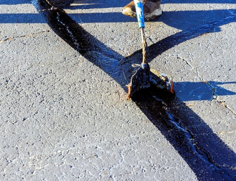 Hot rubberized crack sealant being squeegeed across a freshly cleaned asphalt seam