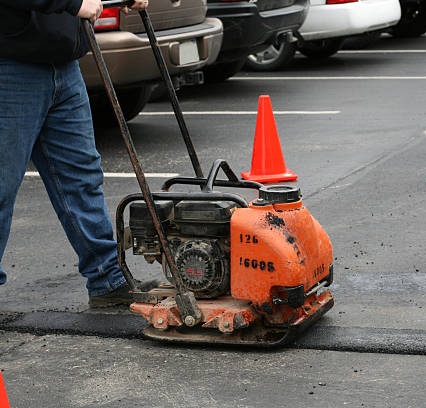 Plate compactor finishing a fresh hot-mix asphalt patch in a parking lot
