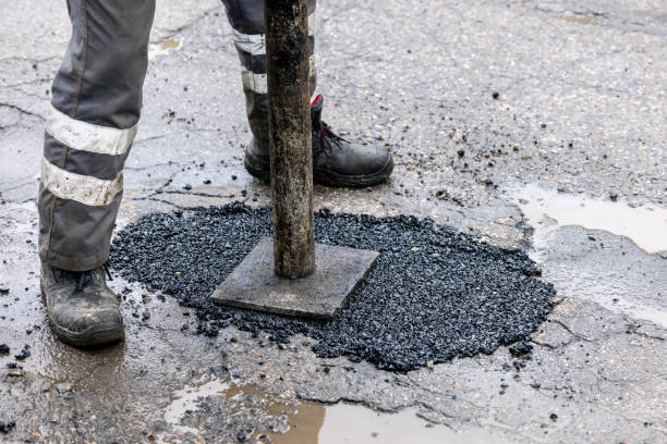 Crew member tamping fresh hot-mix asphalt into a pothole on a city street